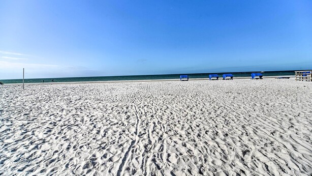 A sandy beach with blue chairs and a lifeguard tower.