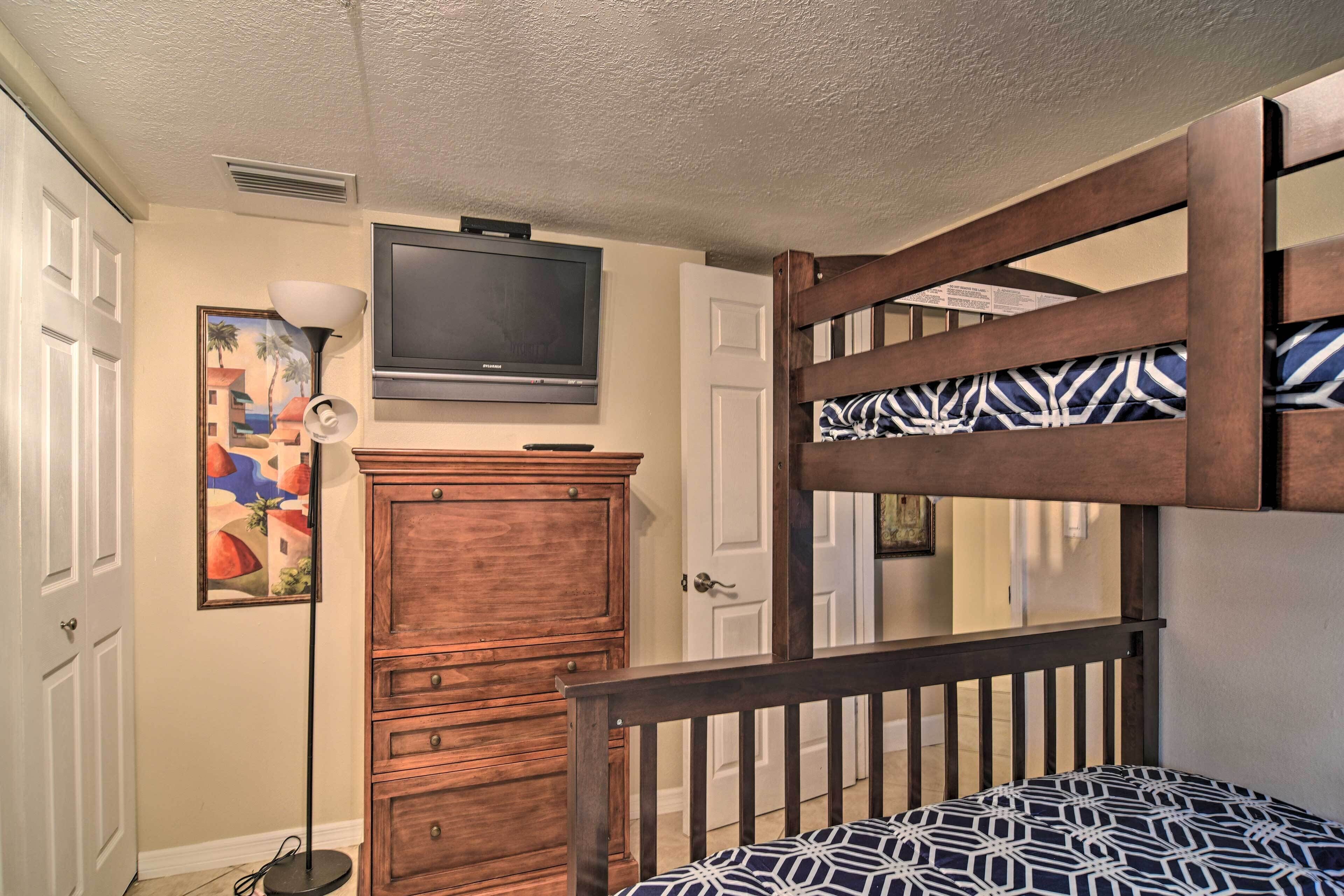 A bedroom with a bunk bed, a dresser, a television mounted on the wall, and a painting on the wall.