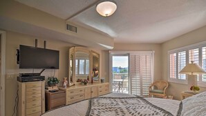 A bedroom with a bed, dresser, TV, and a balcony with a chair.