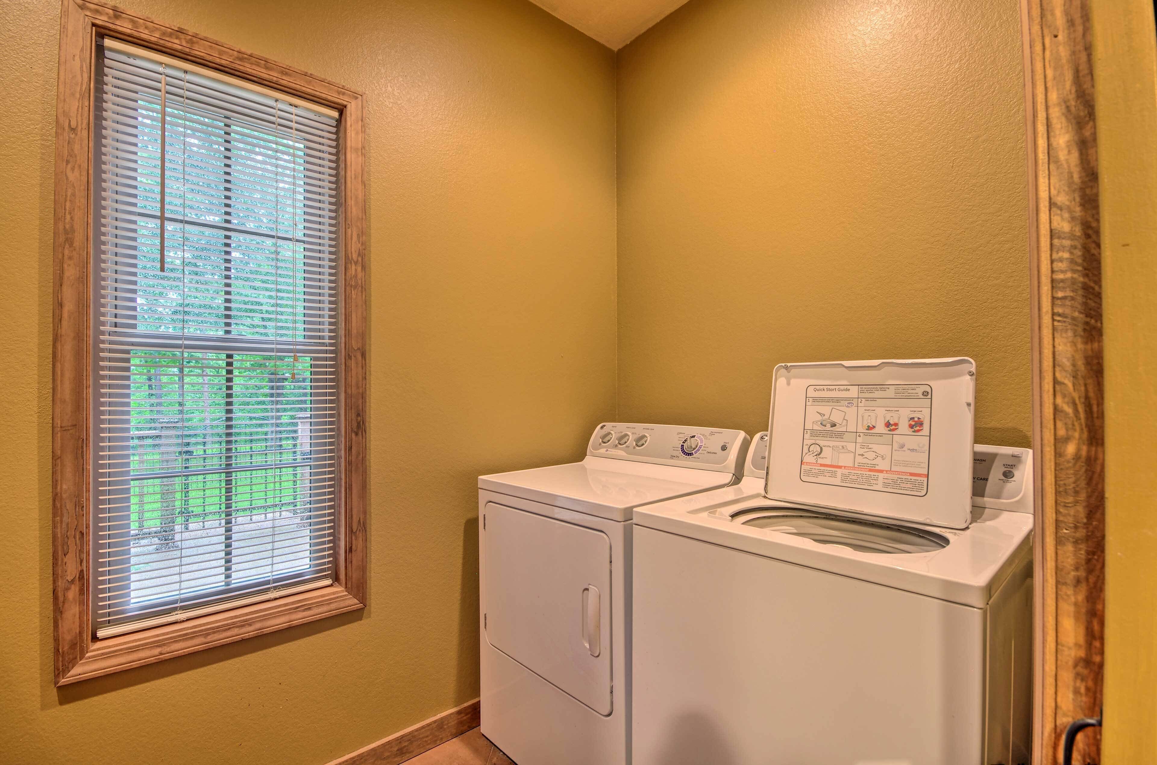 A laundry room with a washer and dryer, a window with blinds, and a wooden frame around the window.