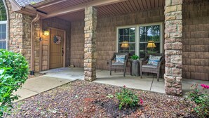 Une maison avec une façade en pierre, une porte d’entrée en bois et deux fauteuils en osier avec des coussins.