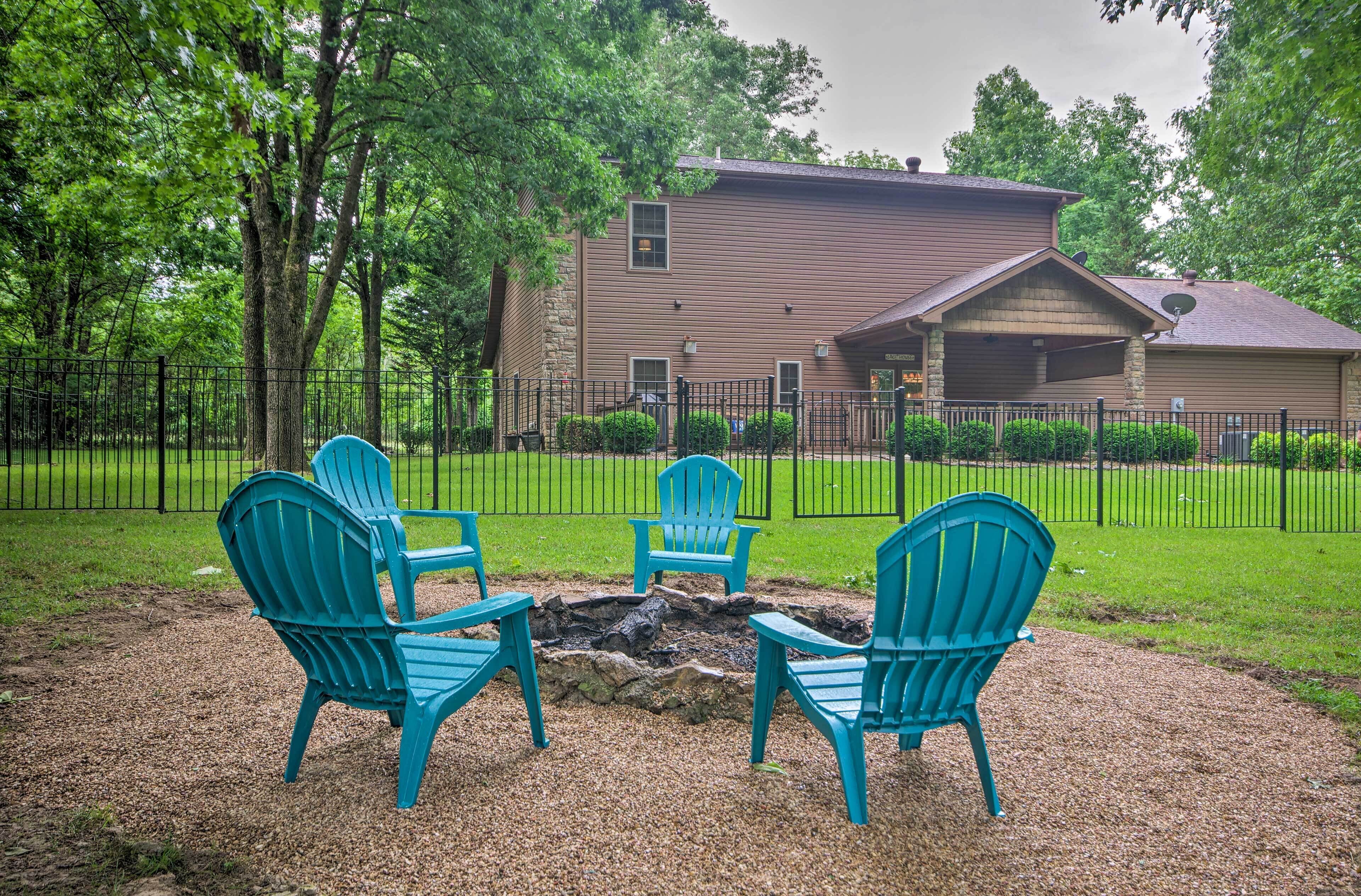 A house with a stone foundation and a brown exterior, surrounded by a black fence and lush greenery.