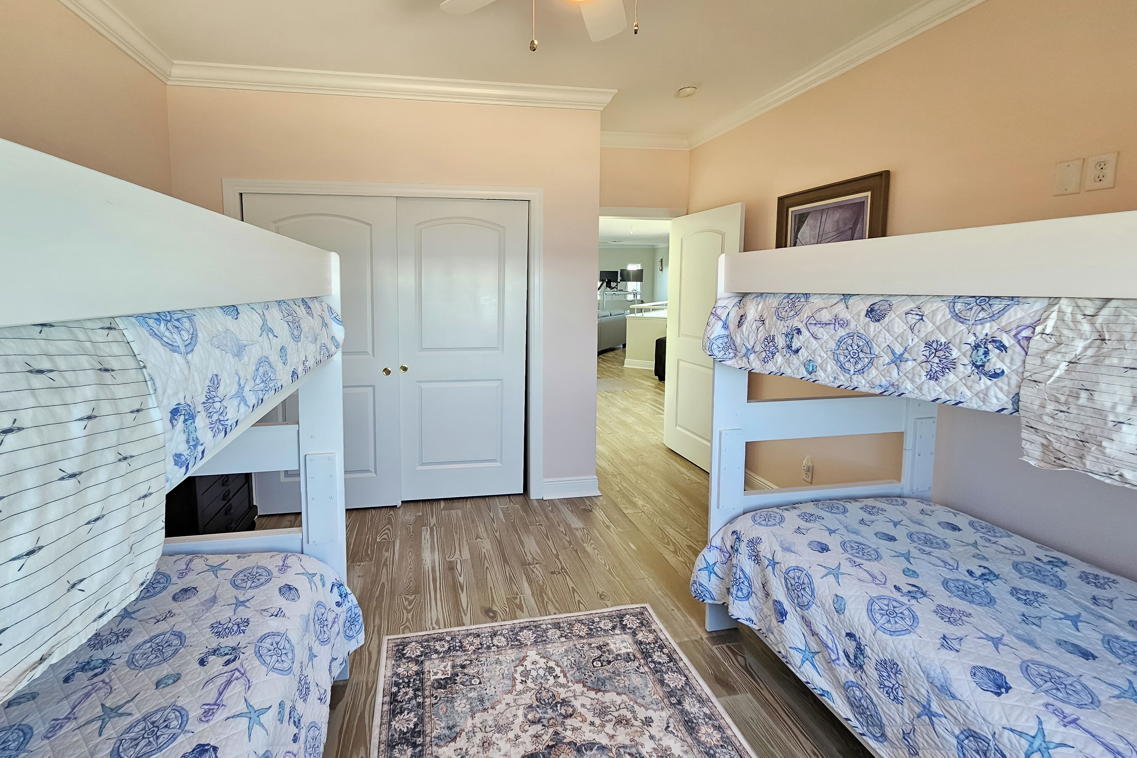 A room with bunk beds, a wooden floor, a patterned rug, and a door leading to a kitchen.