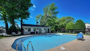 A swimming pool with lounge chairs, a covered patio, and a building with a chimney.