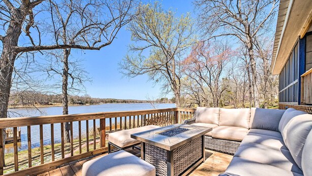 A wooden deck with a sofa, ottoman, and a table with a fire pit. - Lakefront Fort Towson Home: Private Dock & 3 Decks (Fort Towson)
