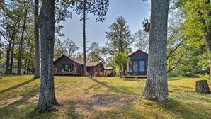 A cabin with a wooden deck, surrounded by tall trees and a grassy yard. - Cabin on Rush Lake w/ Bar, Grill & Kayaks! (Atlanta)