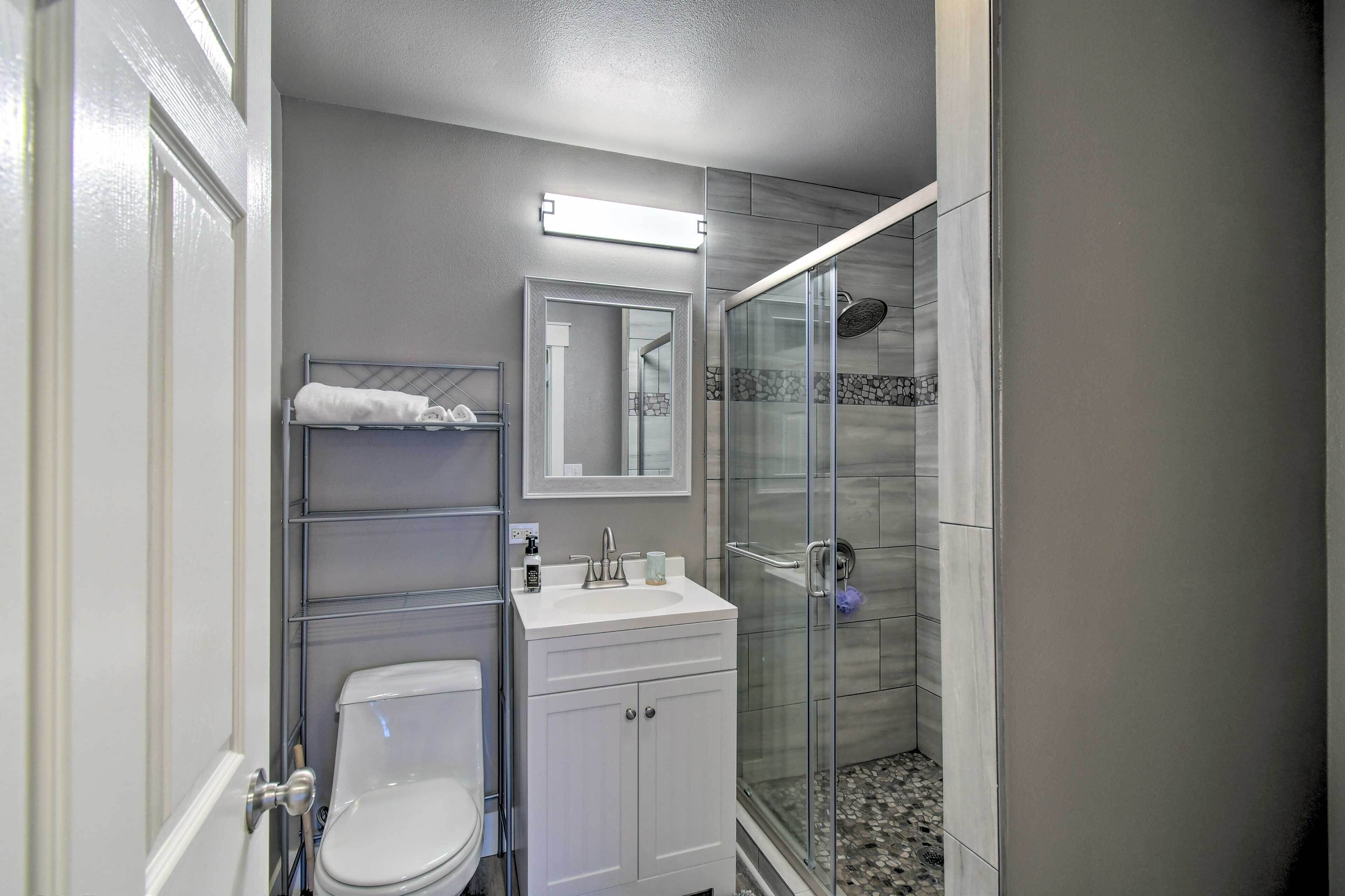 Une salle de bain comprenant des toilettes, un lavabo, un miroir et une douche fermée par une paroi de verre.