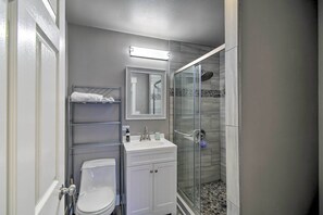 A bathroom with a toilet, a sink, a mirror, and a glass-enclosed shower. - Scenic & Spacious Getaway on North Bay w/ Deck! (Allyn)
