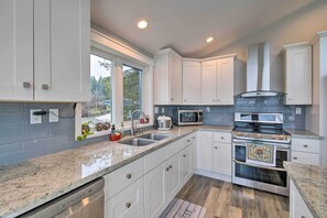 A modern kitchen with white cabinets, granite countertops, a built-in oven, and a window providing natural light. - Scenic & Spacious Getaway on North Bay w/ Deck! (Allyn)
