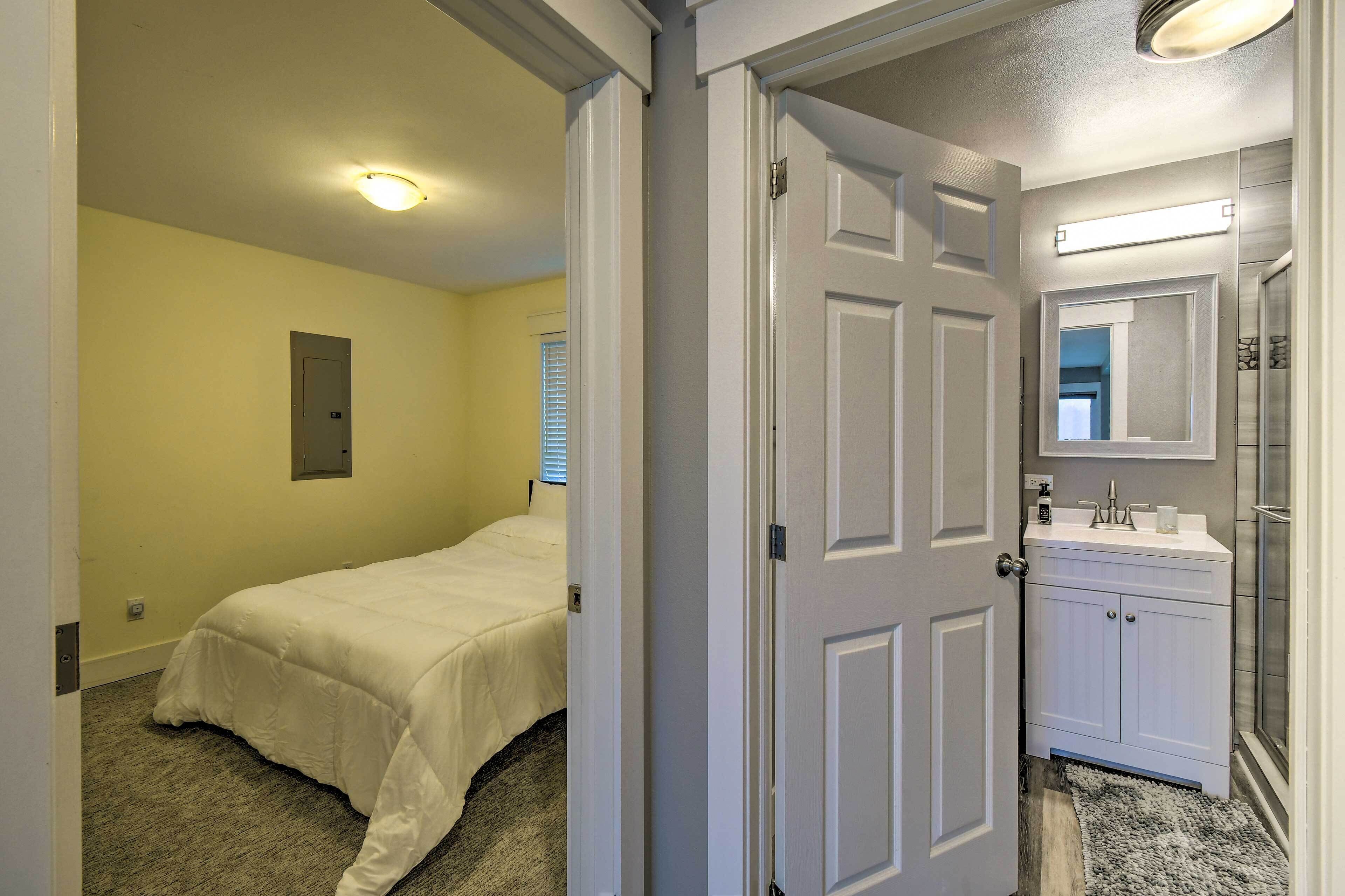 A bedroom with a bed, a door leading to a bathroom with a sink and mirror.