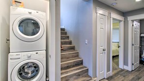 A laundry room with stacked washers and dryers, a staircase leading to a bedroom, and a bathroom with a toilet and sink. - Scenic & Spacious Getaway on North Bay w/ Deck! (Allyn)