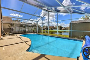 A clear blue swimming pool with a covered patio area, surrounded by a fence and a view of a residential neighborhood. - Lake-view Home w/ Game Room in Orlando! (Kissimmee)