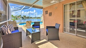 A covered patio with wicker furniture, a glass table, and a view of a swimming pool and greenery. - Lake-view Home w/ Game Room in Orlando! (Kissimmee)