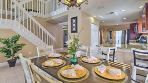 A dining area with a wooden table set for six, white chairs, a chandelier, and a staircase in the background. - Lake-view Home w/ Game Room in Orlando! (Kissimmee)