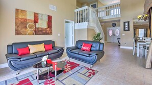 A spacious living area with two black leather sofas, a coffee table, and a large abstract painting on the wall. A staircase leads to an upper level. - Lake-view Home w/ Game Room in Orlando! (Kissimmee)