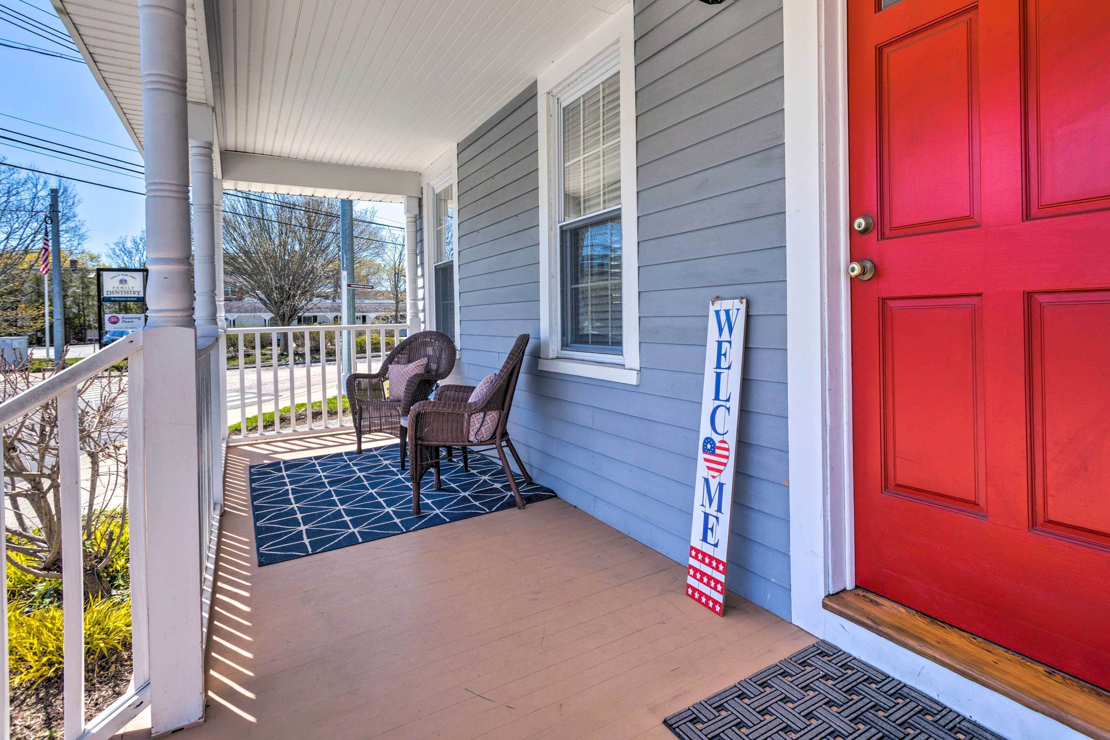 A porch with a red door, a welcome sign, and a covered seating area.
