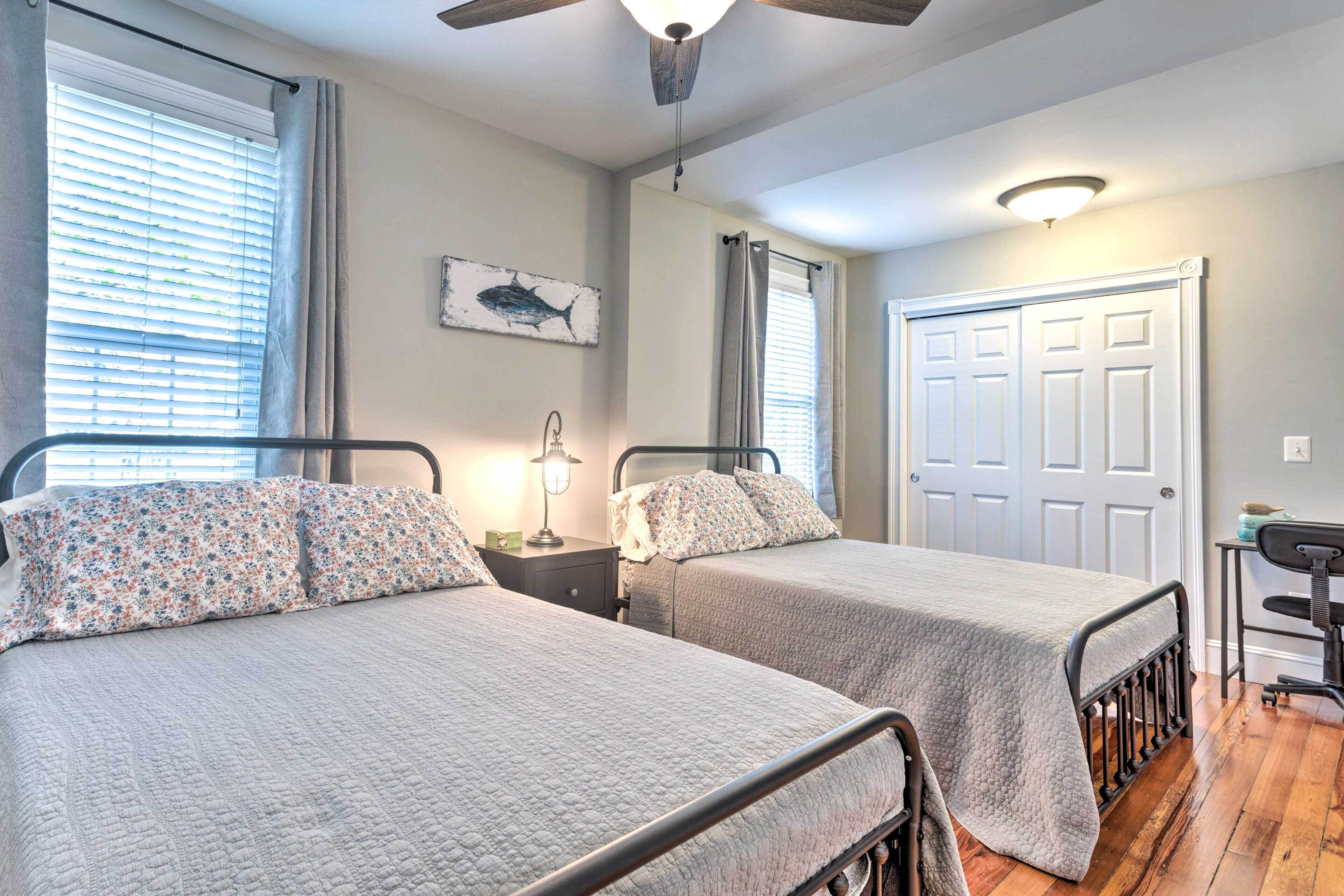 A bedroom with two beds, a ceiling fan, a desk, and a door.