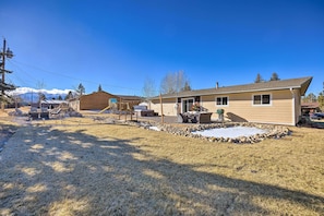 A single-story house with a patio area, outdoor seating, and a view of snow-capped mountains in the background.
