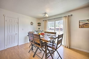 A dining area with a wooden table and chairs, a ceiling light fixture, and a window with curtains.