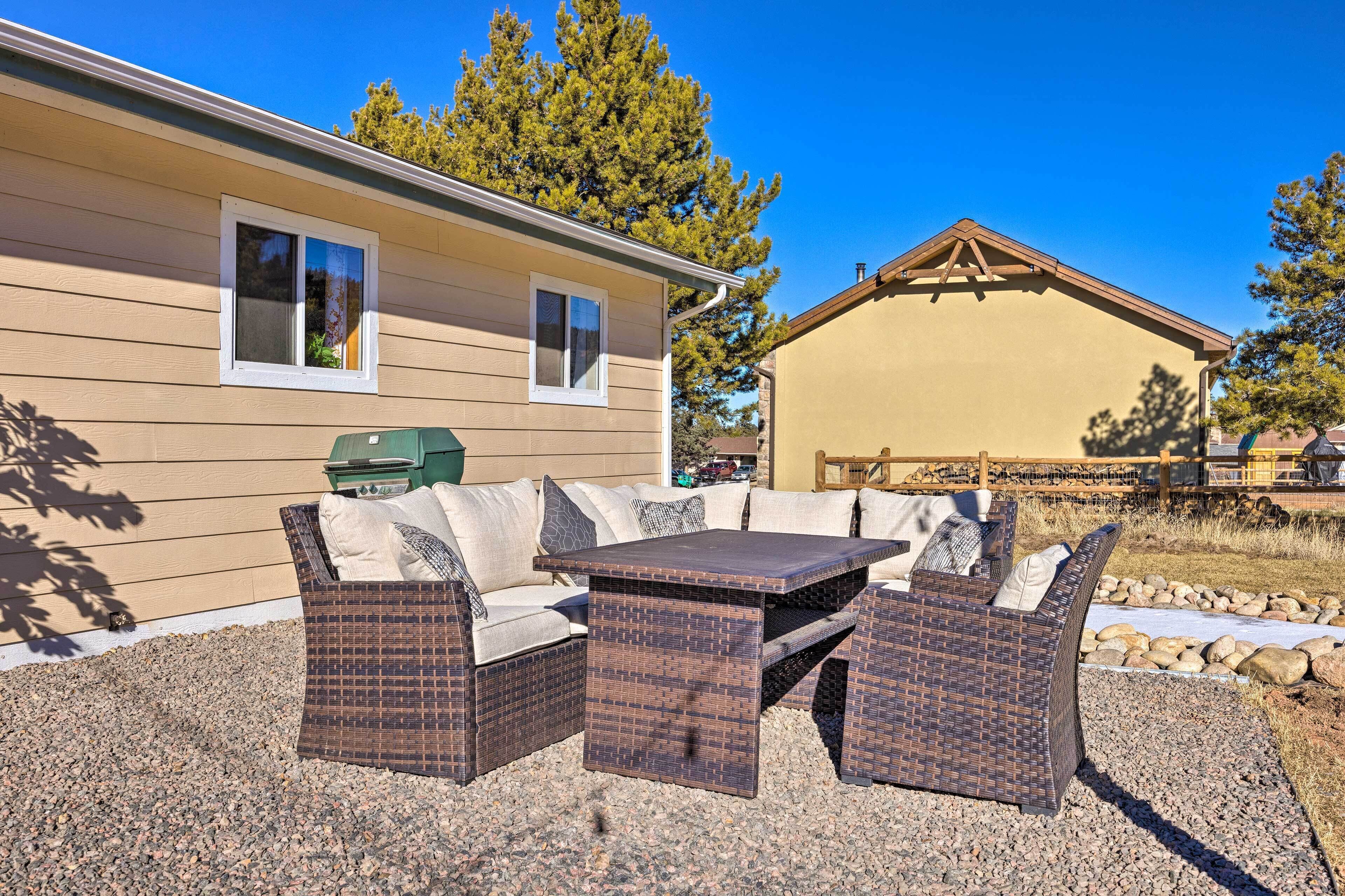 A patio with wicker furniture, a grill, and a house with beige siding and a wooden deck.