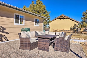 An outdoor patio with wicker furniture, a grill, and a house in the background.