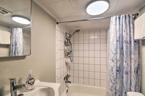 A bathroom with a bathtub, a sink with a soap dispenser, a shower with a curtain, and a mirror.