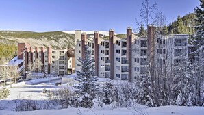Un hotel de varios pisos con un diseño arquitectónico moderno, con una combinación de fachadas de ladrillo y blancas, rodeado de árboles y colinas cubiertas de nieve.