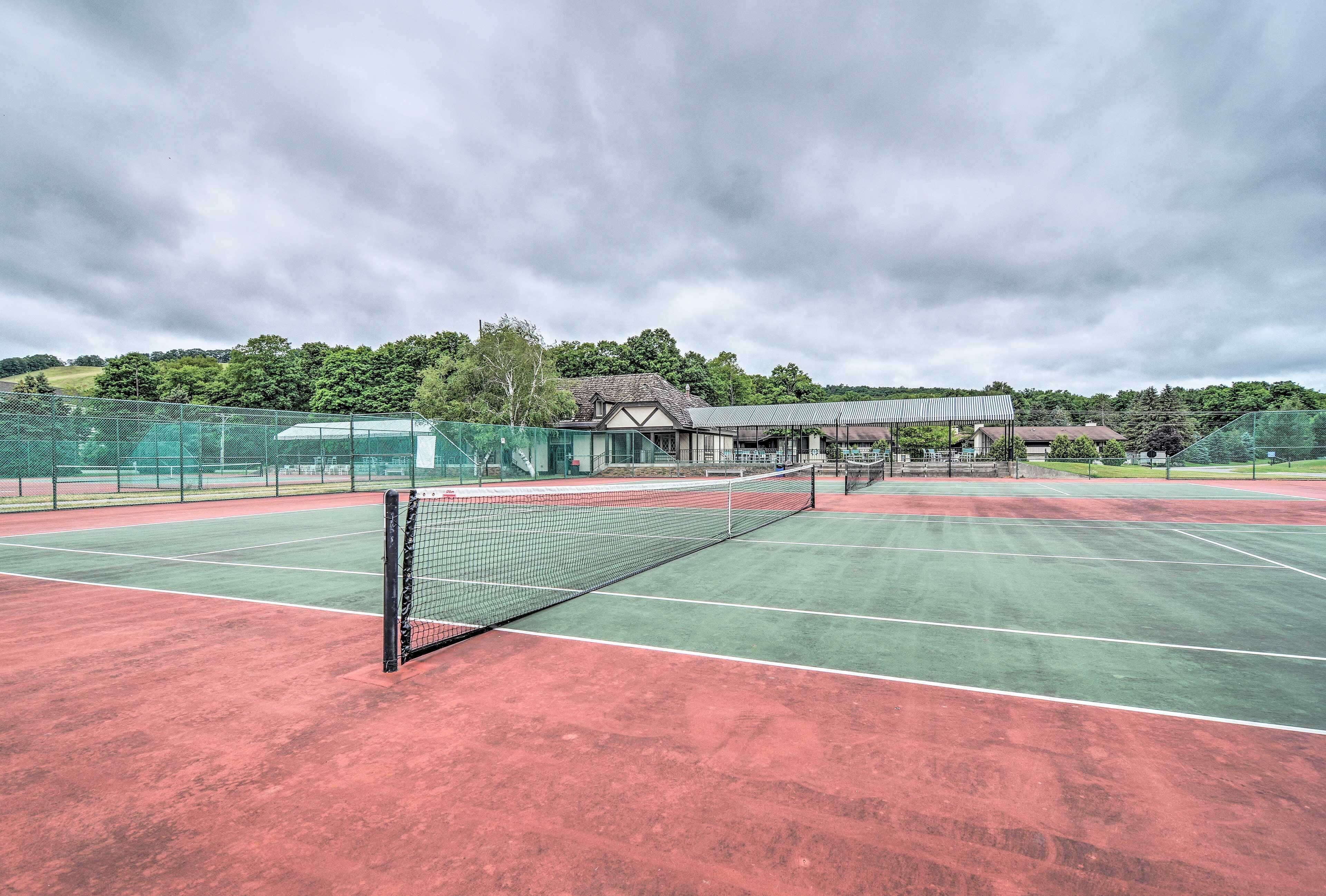 A tennis court with a net, surrounded by a fence and a building in the background.