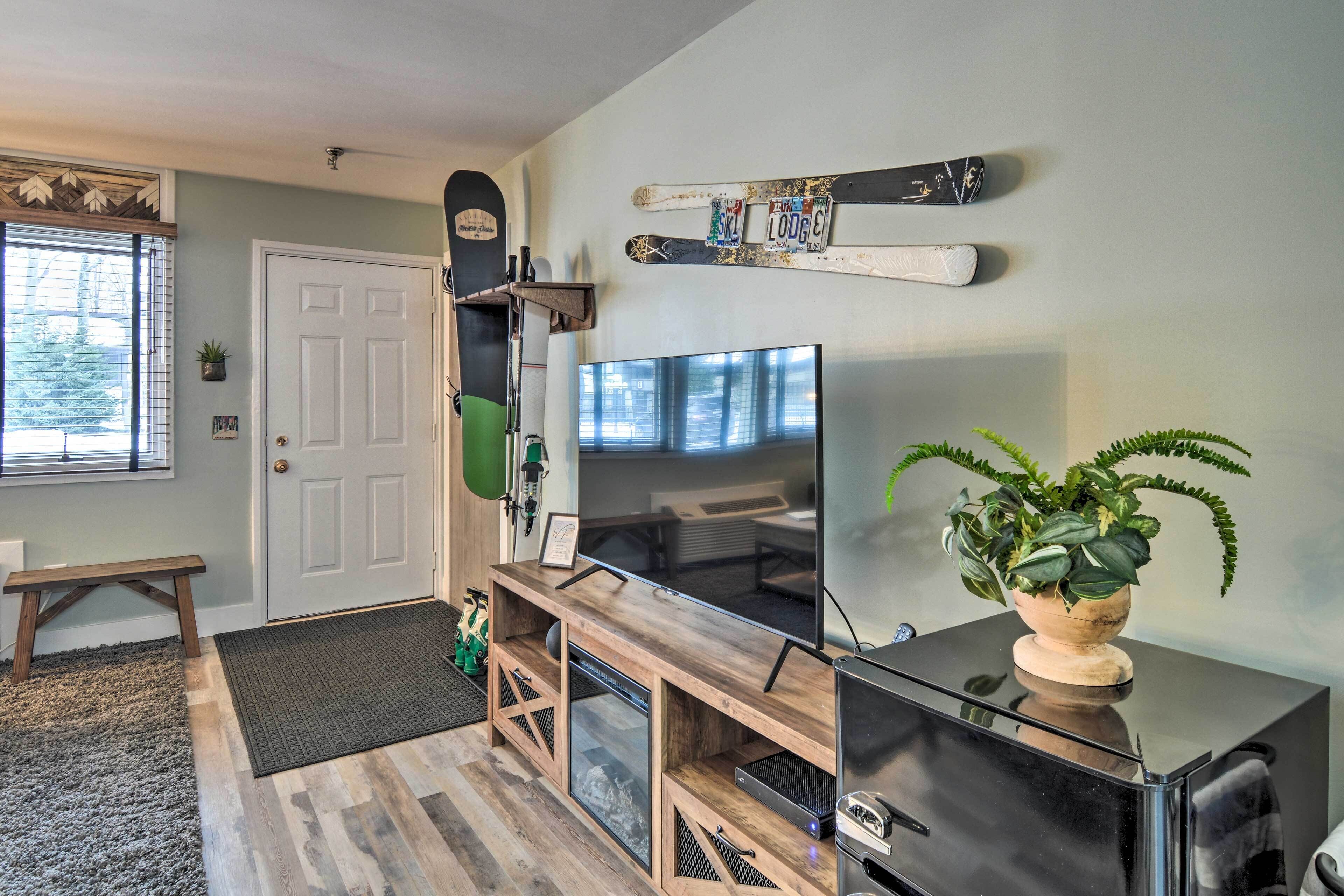 Un soggiorno con televisione, mobile porta TV in legno, sci appesi al muro e una pianta in vaso.