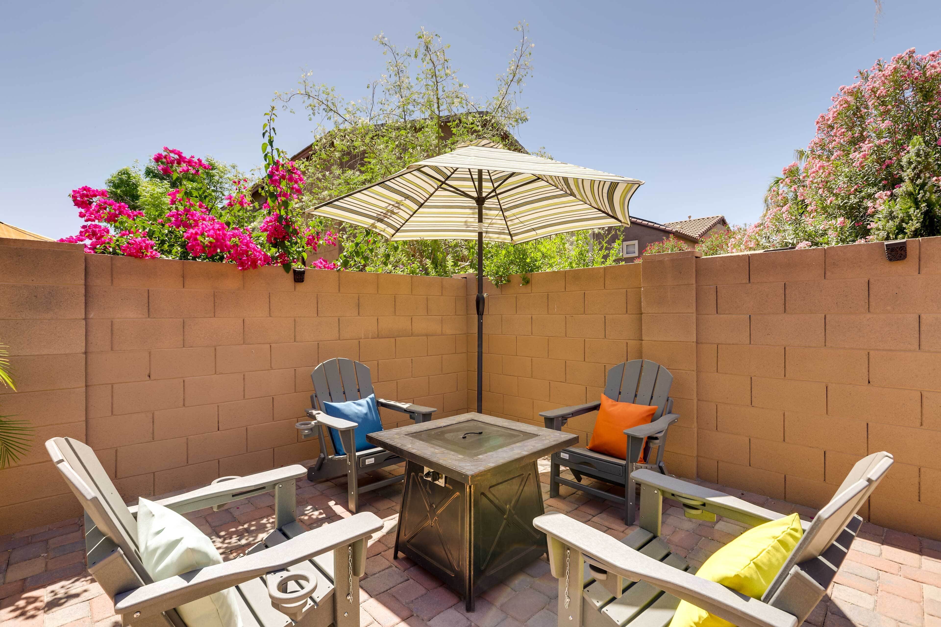 Une terrasse extérieure avec une table à plateau en verre, deux fauteuils Adirondack et un parasol à rayures.