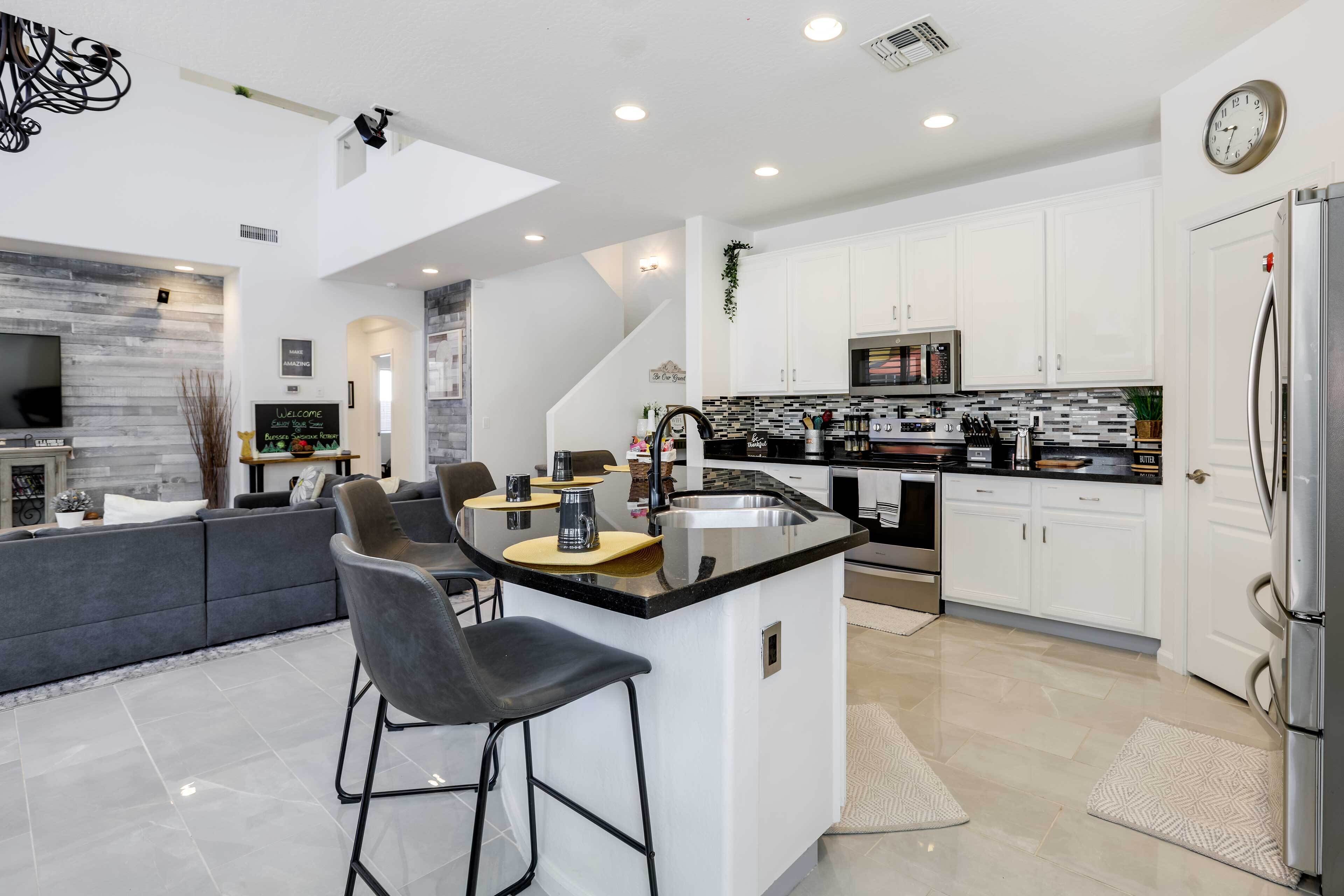 A modern kitchen with white cabinets, a stainless steel refrigerator, and a built-in island with bar stools.