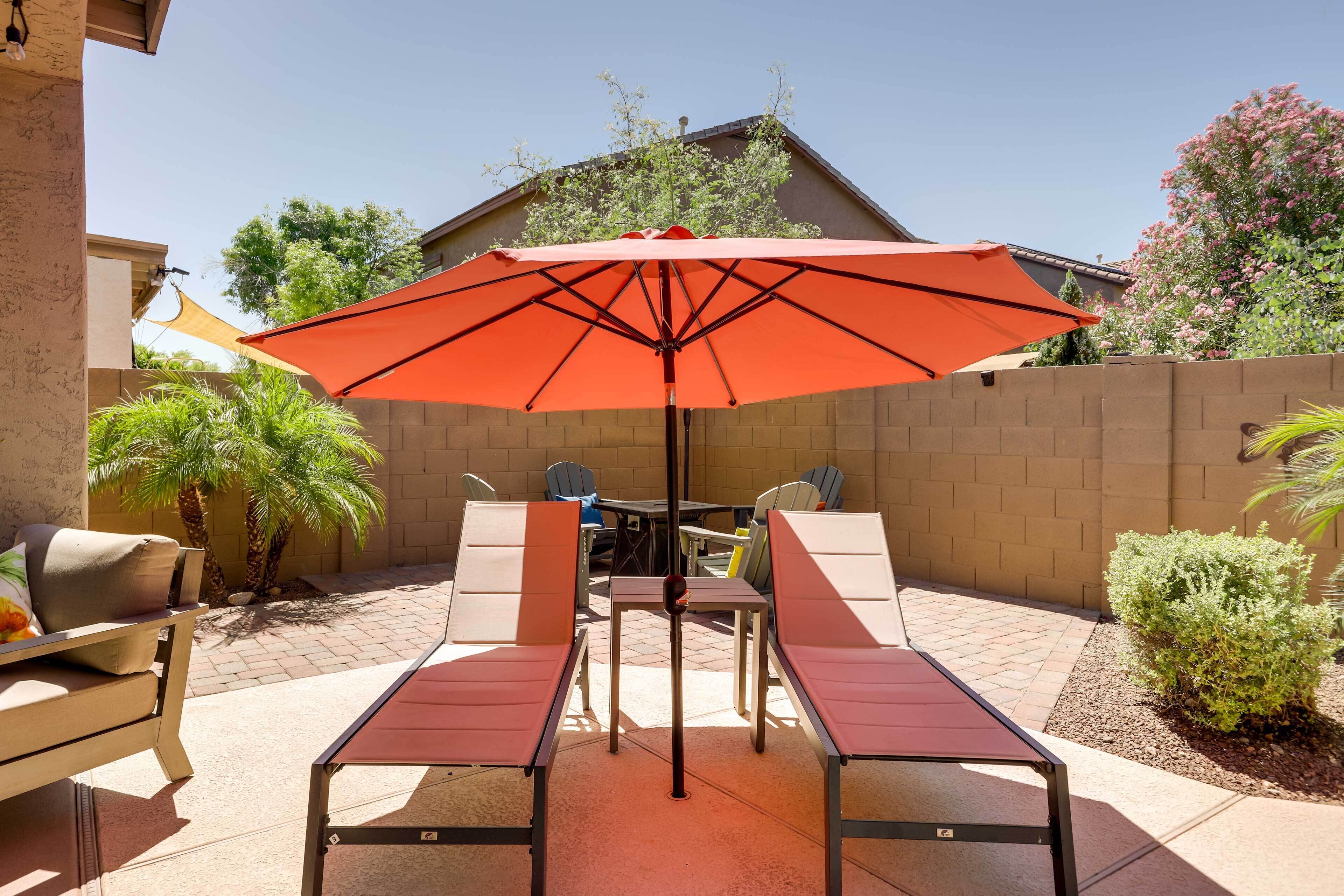 Un patio al aire libre con dos sillones, una mesa y un paraguas rojo.