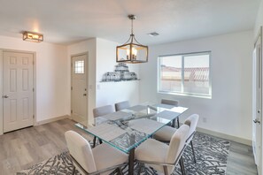 A dining area with a glass table, six chairs, a chandelier, a patterned rug, and a window with blinds. - Putting Green, Pool Access: Lake Havasu City Home! (Lake Havasu City)