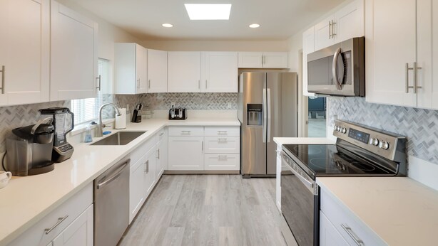 A modern kitchen with white cabinets, stainless steel appliances, and a herringbone-patterned backsplash. - Putting Green, Pool Access: Lake Havasu City Home! (Lake Havasu City)