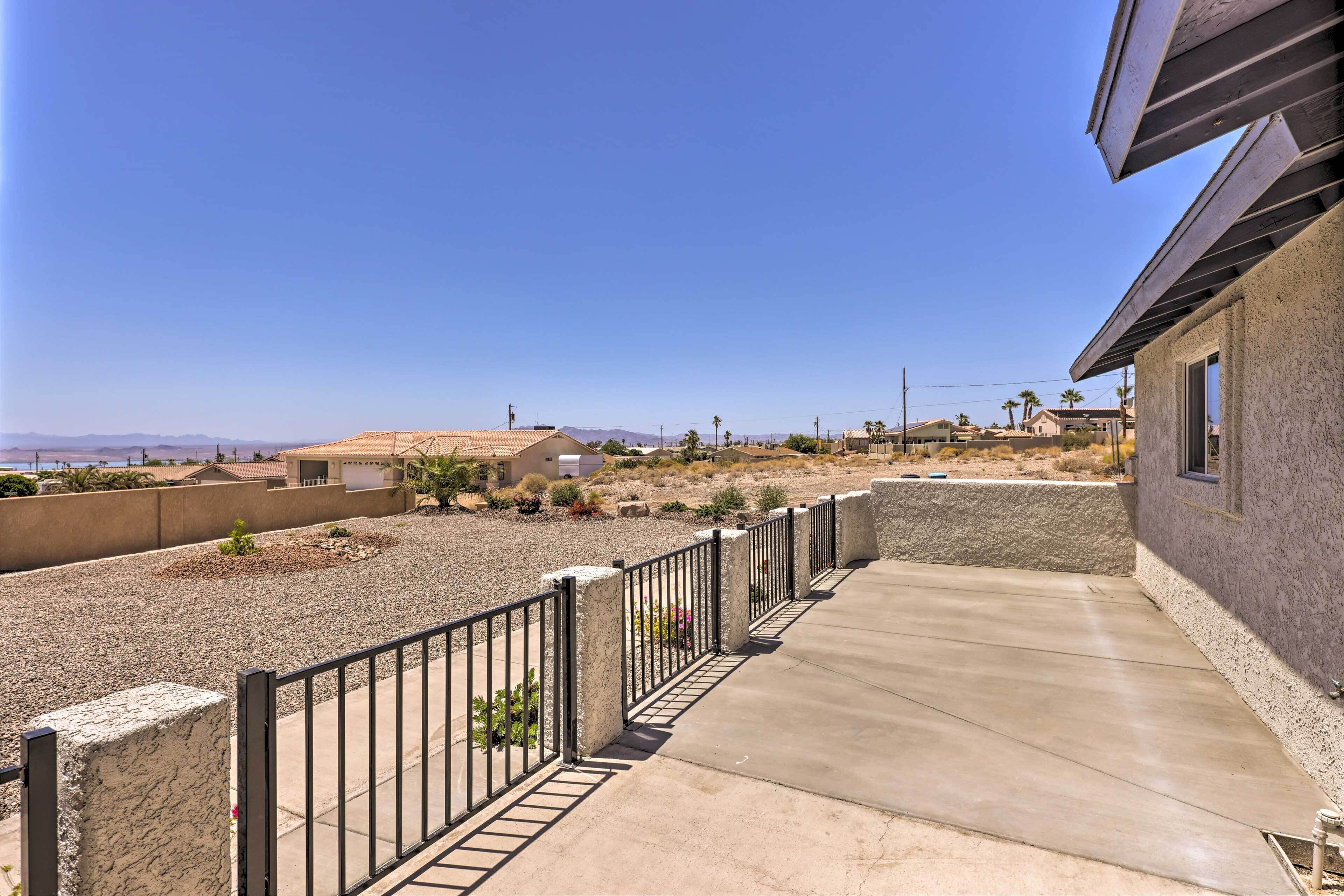 A residential property with a concrete patio, a metal fence, and a view of a desert landscape with distant mountains.