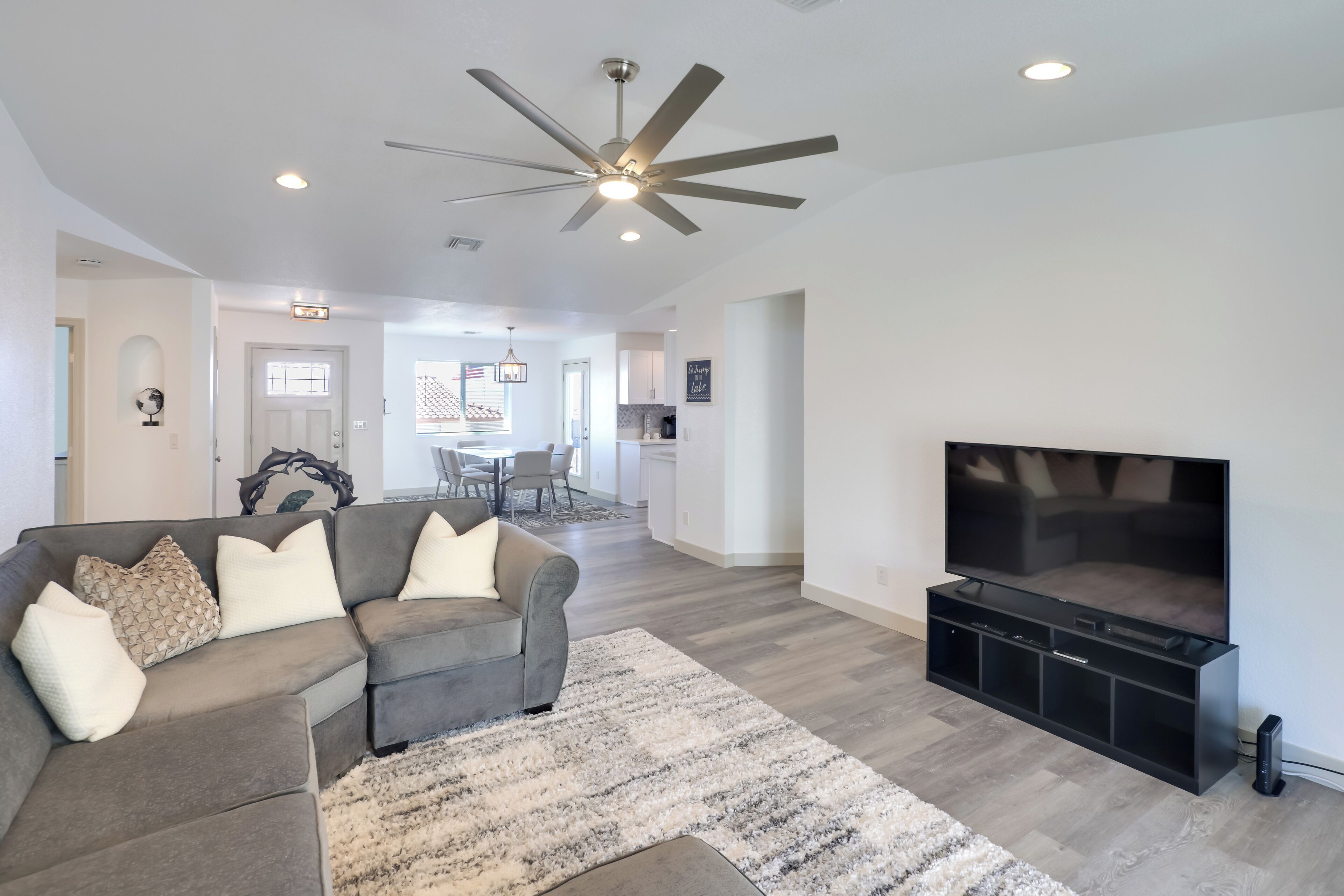 A modern living room with a sectional sofa, a flat-screen TV, and a ceiling fan.