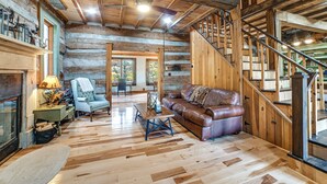 Ein rustikales Blockhaus-Interieur mit Holzboden, Ledersofa, Essbereich und einer Treppe.