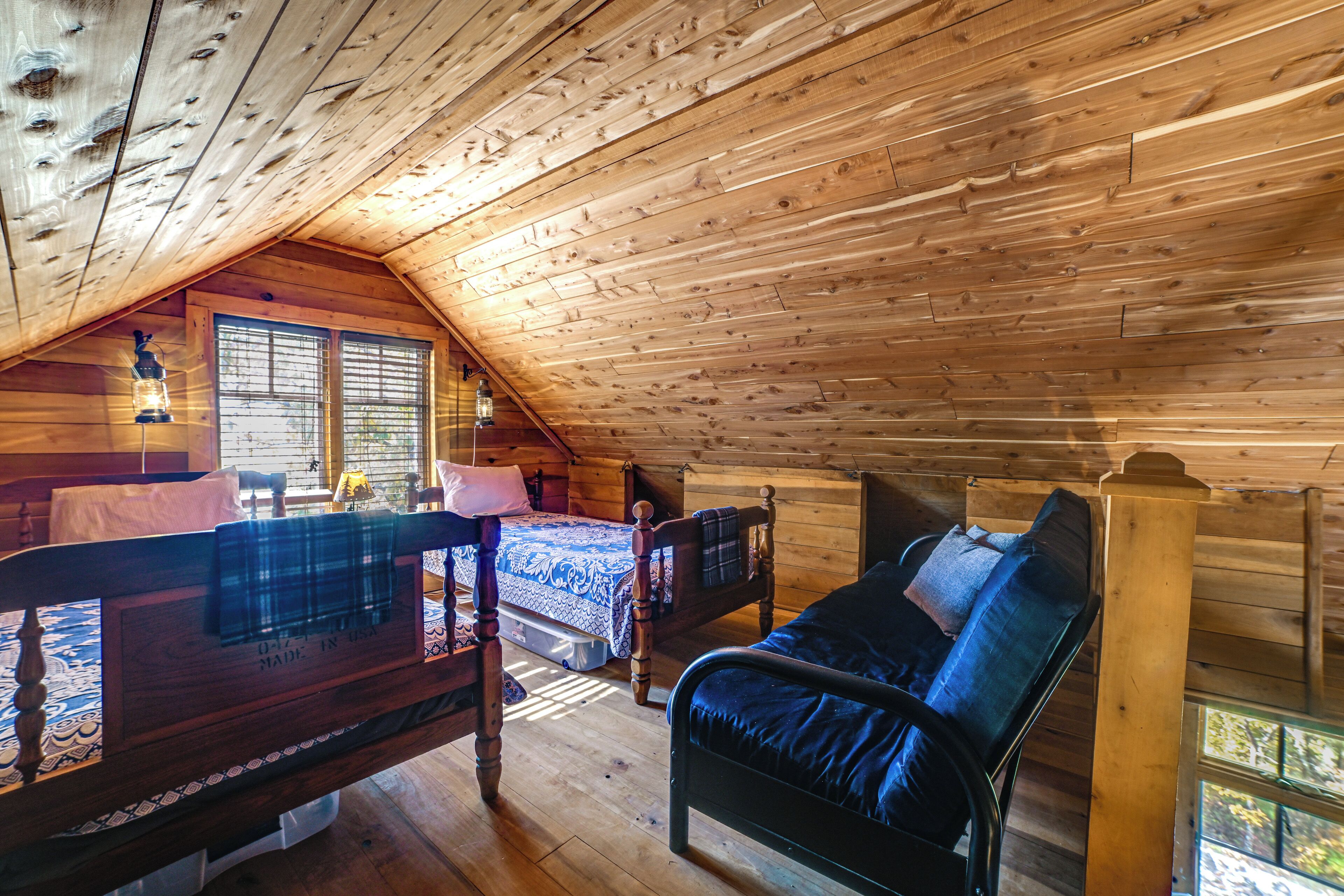 A cozy attic bedroom with a wooden ceiling, a bed, a bench, and a window with blinds.