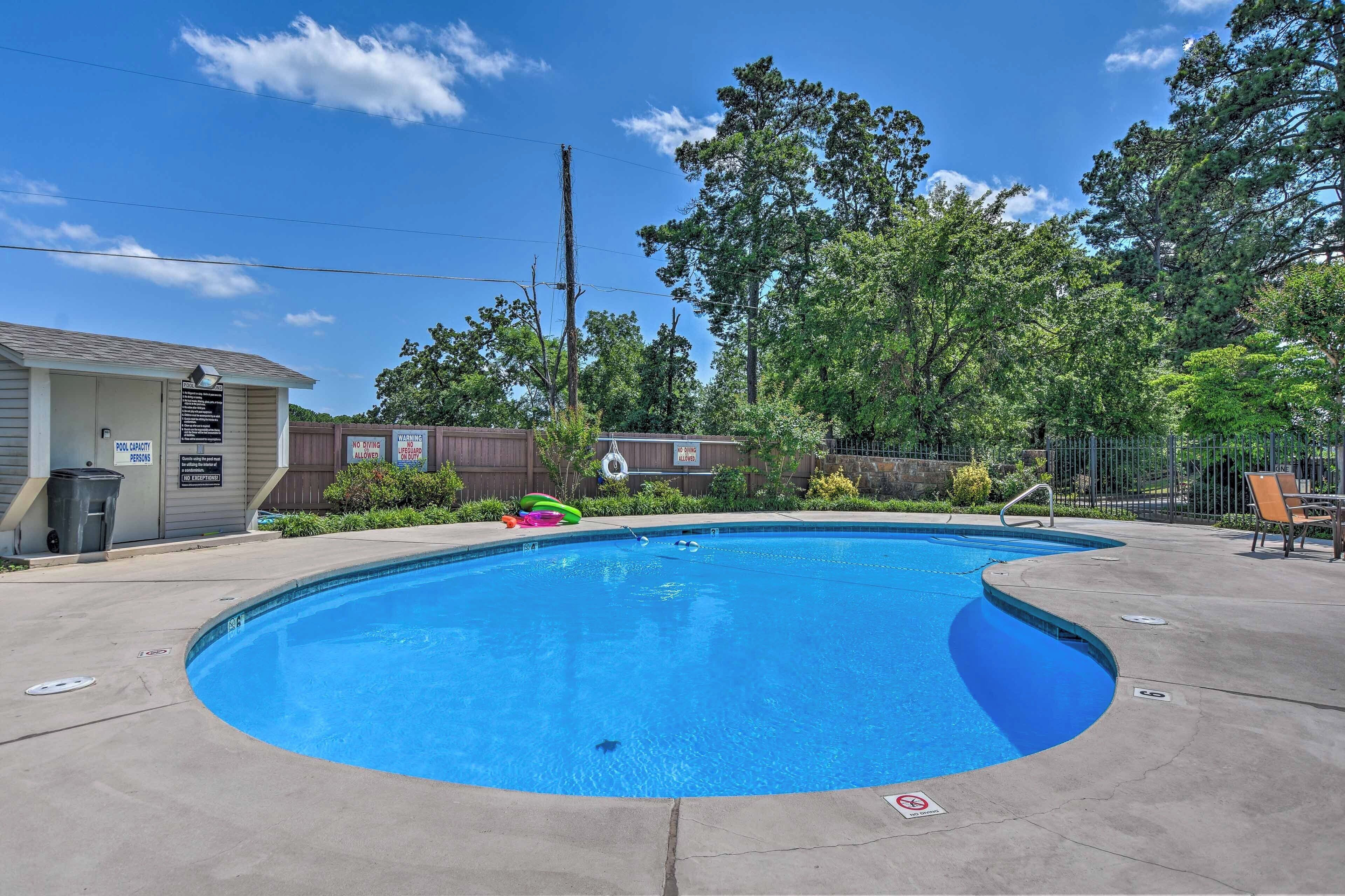 A swimming pool with a wooden deck, surrounded by trees and a fence.