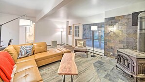 A modern living room with a leather sofa, a wooden coffee table, a stone fireplace, and a large window with blinds.