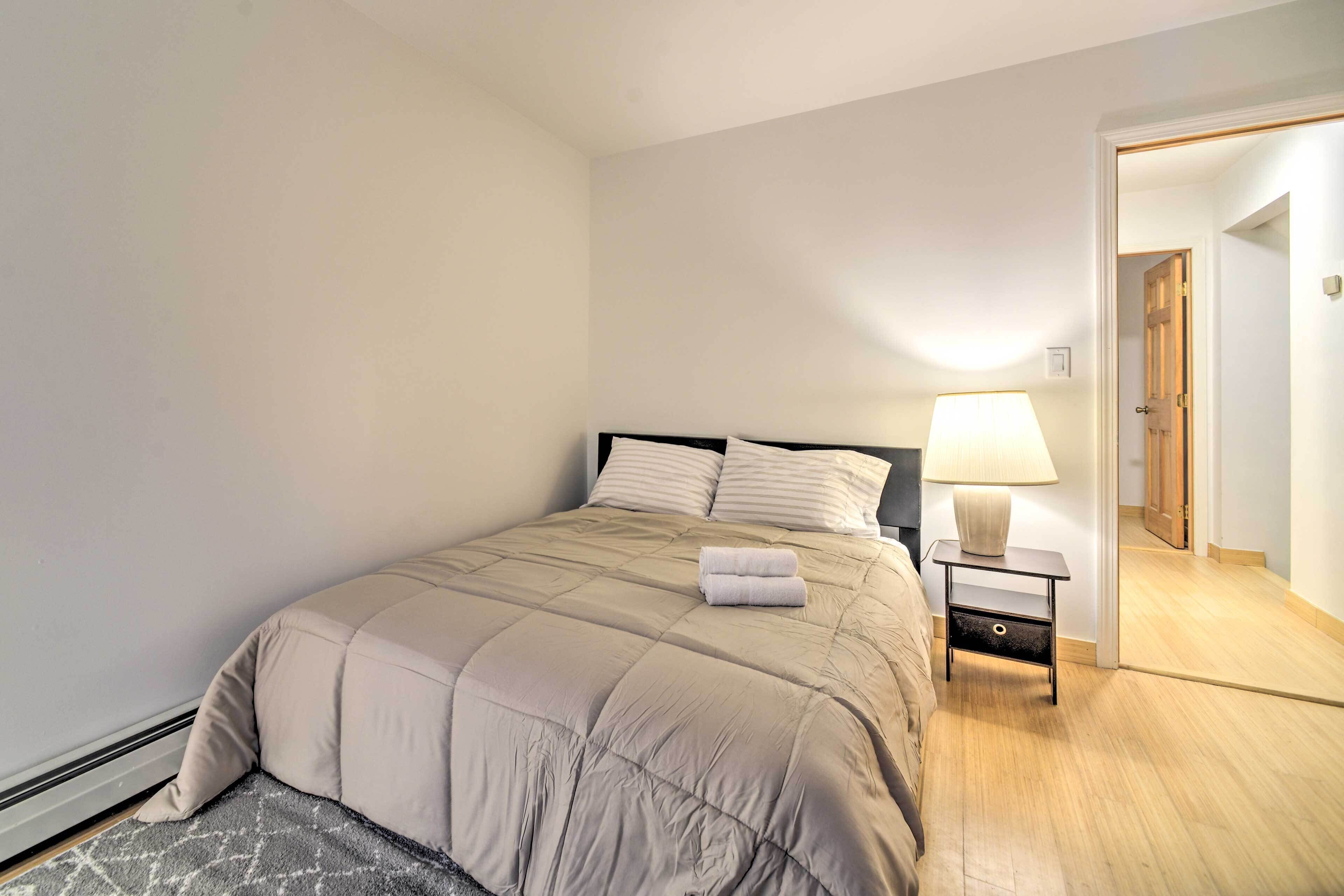 A neatly made bed with a beige comforter and pillows, a bedside table with a lamp, and a wooden floor.