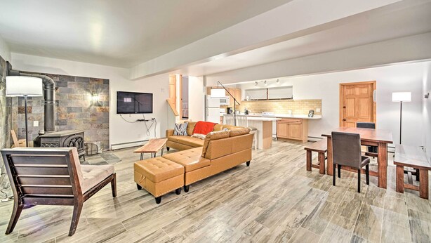 A spacious living area with a sofa, a wooden chair, a dining table with benches, a kitchen in the background, and a stone fireplace.