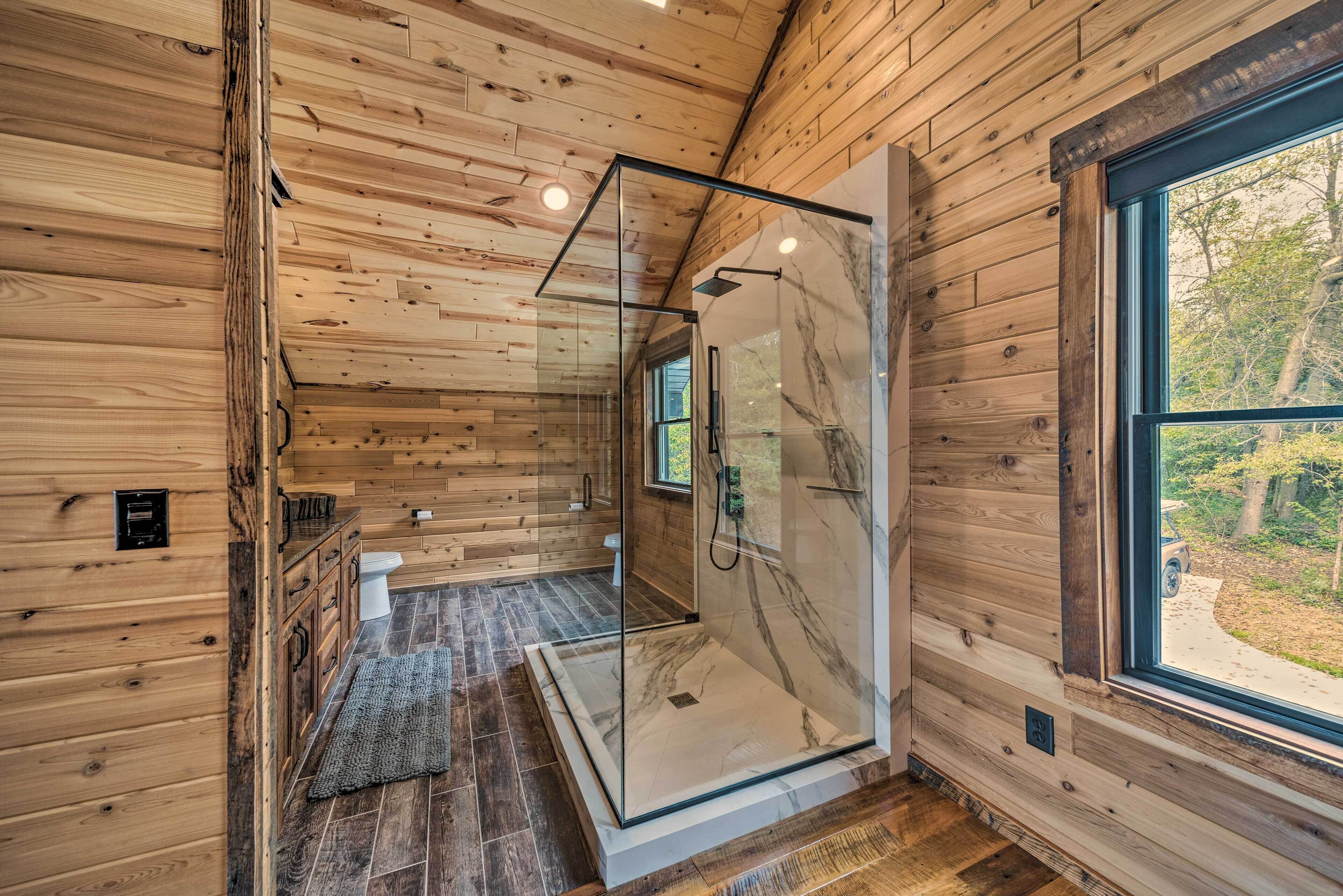 Une salle de bain rustique, avec une cabine de douche en verre, un espace de douche carrelé en marbre et une vue sur l’extérieur grâce à une grande fenêtre.