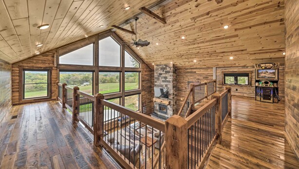 A spacious room with a wooden floor, large windows, a fireplace, and a wooden railing. - Galena Cabin w/ Wraparound Porch & Game Room! (Galena)
