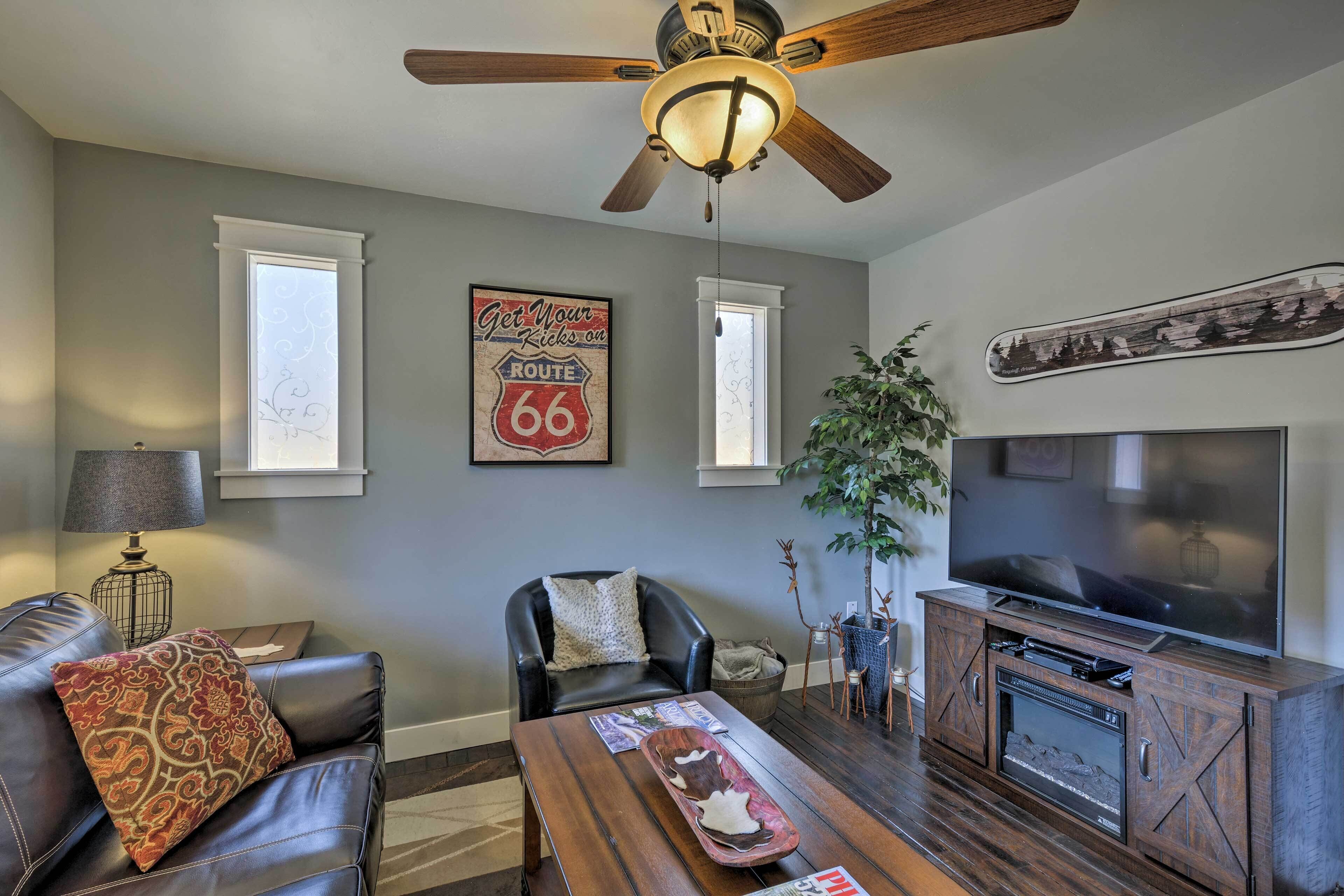 A living room with a ceiling fan, a television, a fireplace, and a Route 66 sign.