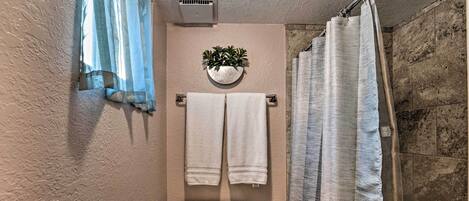 A bathroom with a toilet, two white towels hanging on a towel bar, a potted plant on the wall, and a shower curtain.