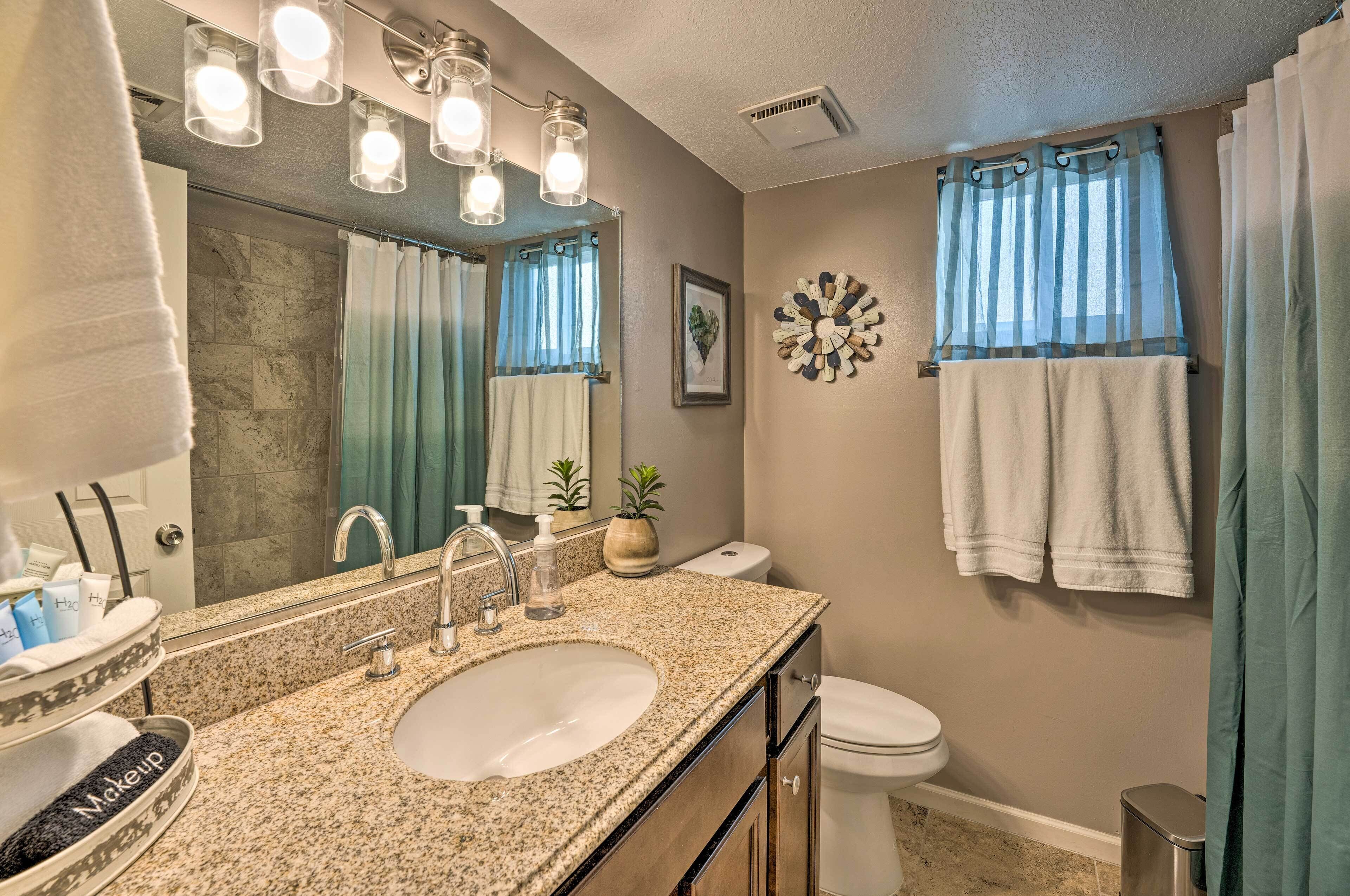 A bathroom with a granite countertop sink, a mirror, a toilet, and a shower curtain.