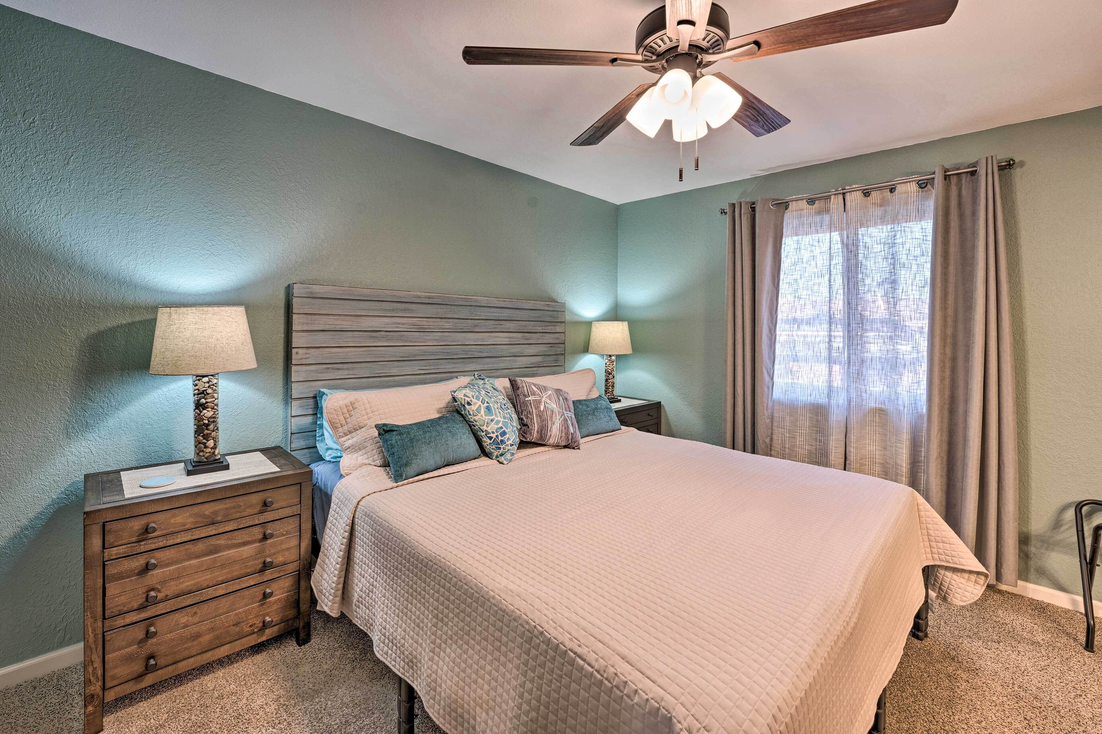 A bedroom with a bed, two nightstands, a ceiling fan, and a window with curtains.