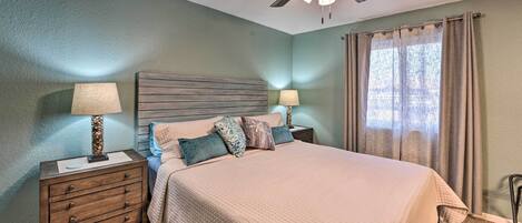 A bedroom with a bed, two nightstands, a ceiling fan, and a window with curtains.