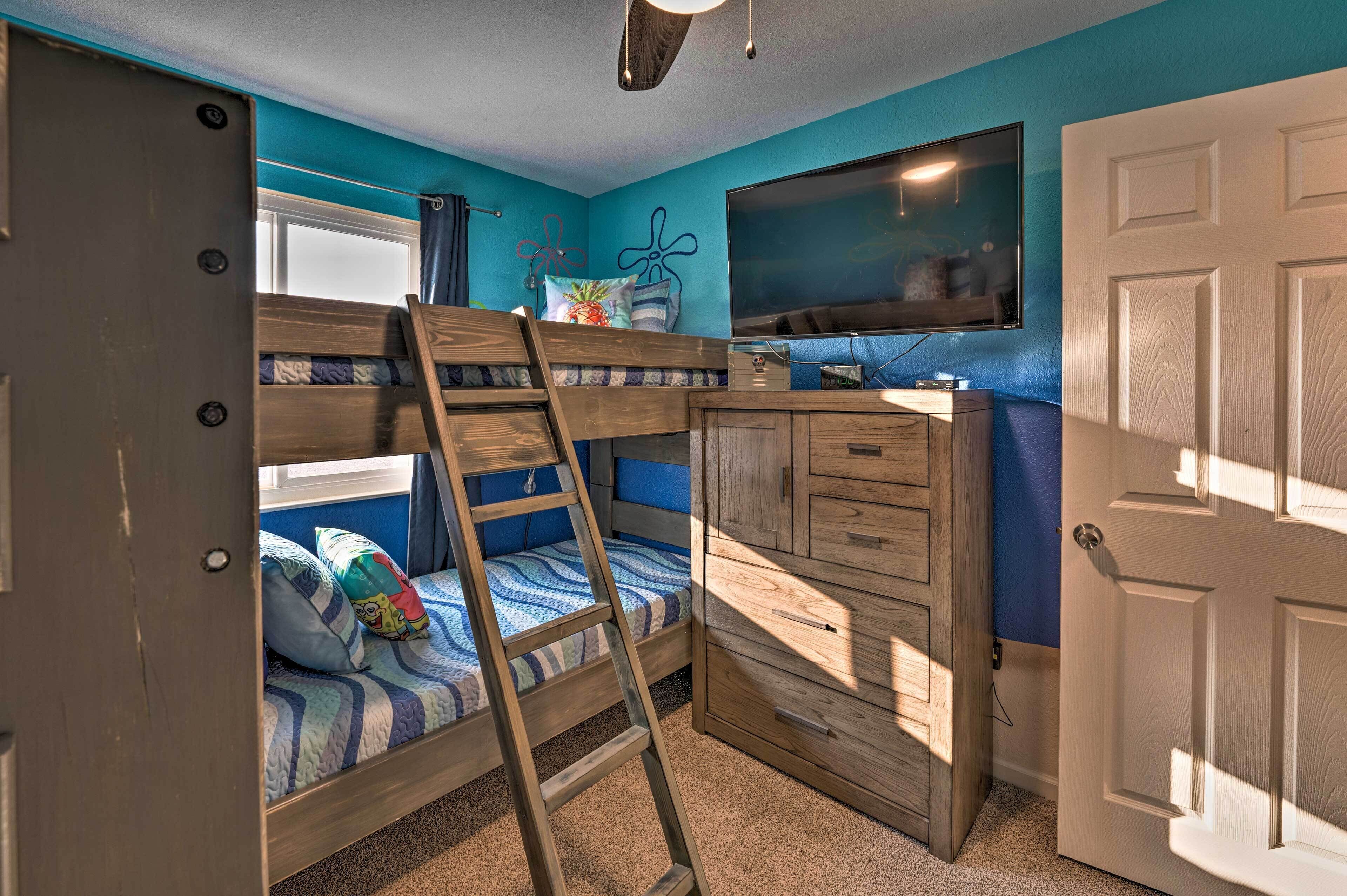 A bunk bed with a ladder, a wooden dresser, and a television on the wall.